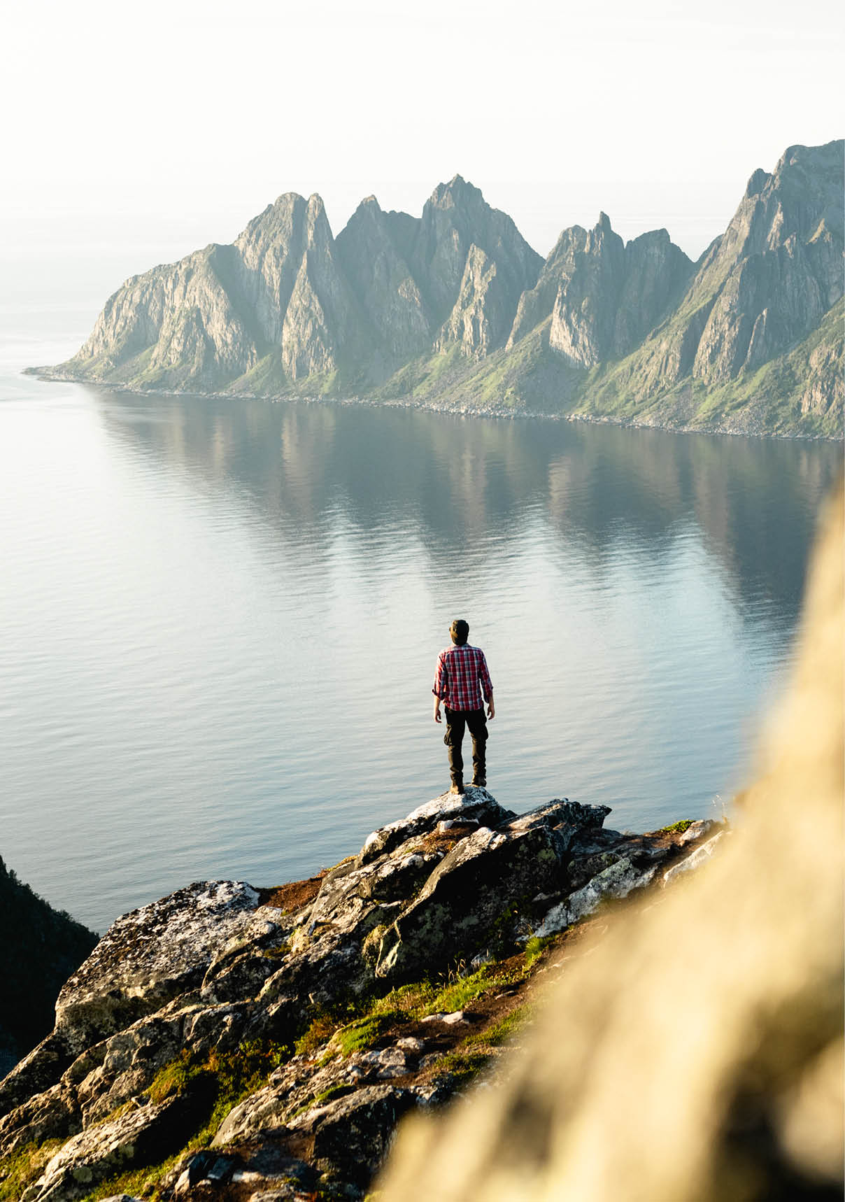 Man contemplating Husfjellet mountain reflected in the fjord standing on top of rocks, Senja island, Troms county, Norway